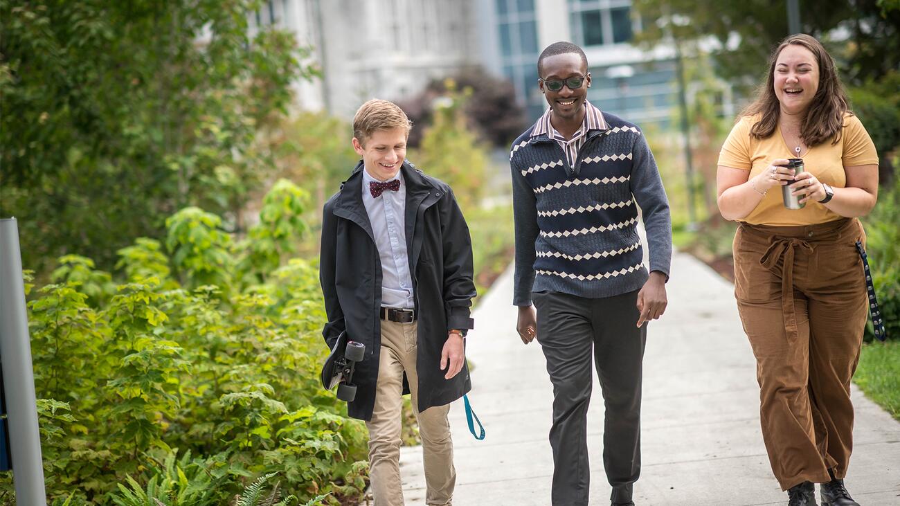 Three colleagues smiling and walking outdoors with greenery on the left