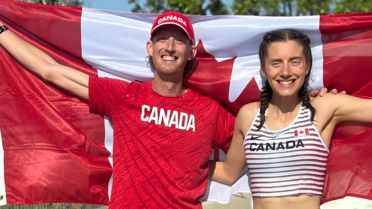 Evan Dunfee and Olivia Lundman, smiling and holding a large Canadian flag behind them