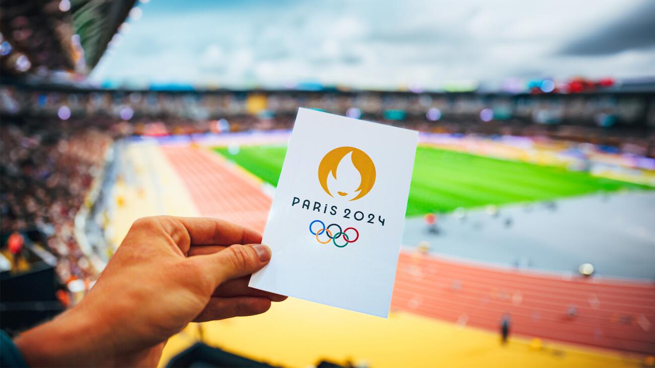 A card reading "Paris 2024" is held in front of a running track