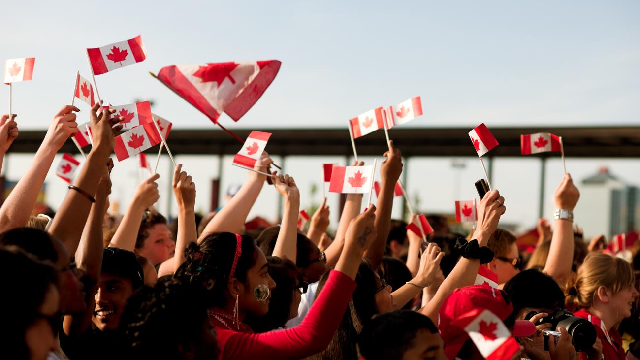 A crowd of people wave Canadian flags