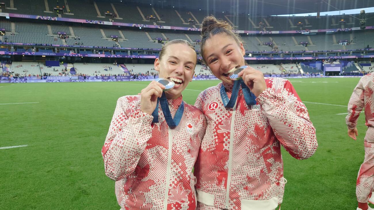 Two female Canadian Olympic athletes on the field showing their silver medals