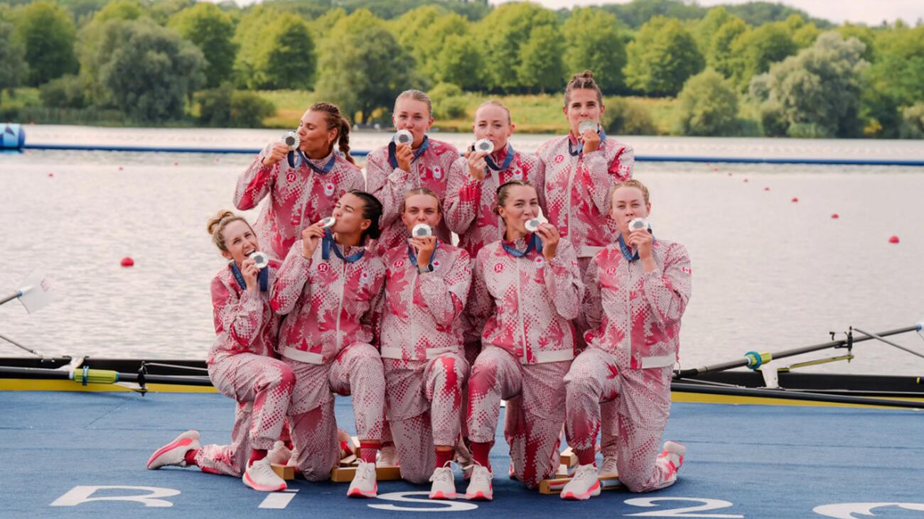 The Canadian women's rowing eight team pose on a dock while kissing their silver medals