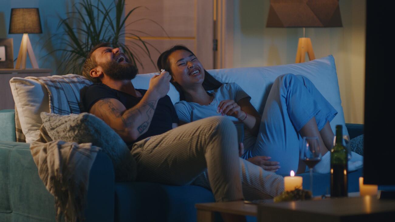 Man and woman laughing on couch in front of TV screen