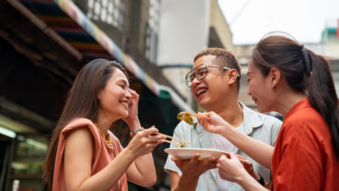 Two women and man eating from a plate with chopsticks