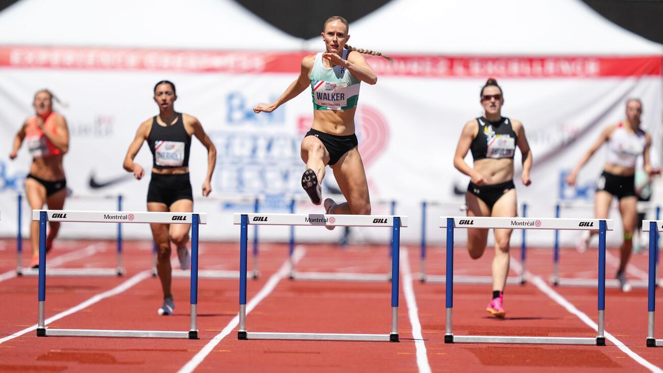 Five track-and-field athletes sprinting down a track with hurdles in each lane