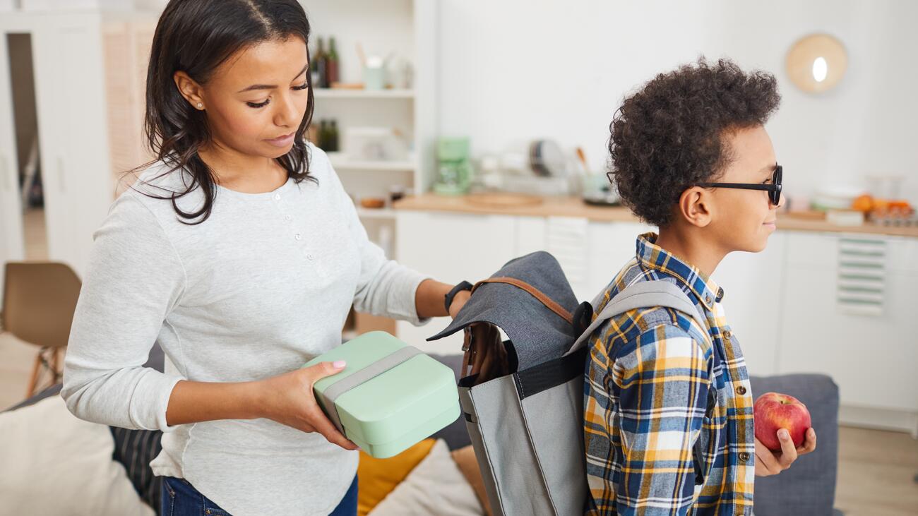 Mother putting lunchbox into boy's backpack