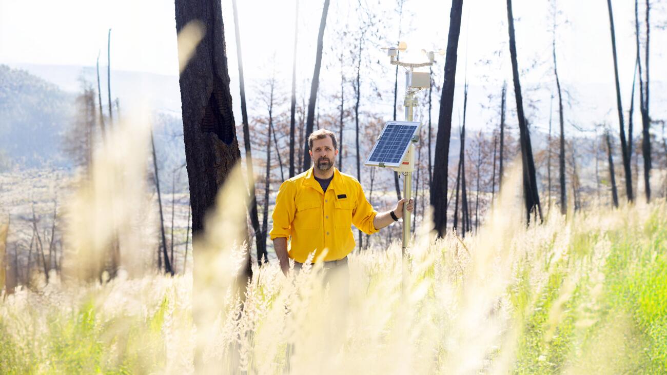 Man standing in field holding pole with devices attached