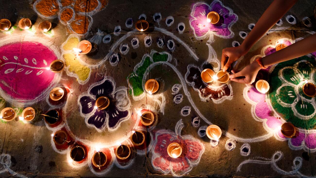 Overhead shot of colourful rangoli and lighted diyas