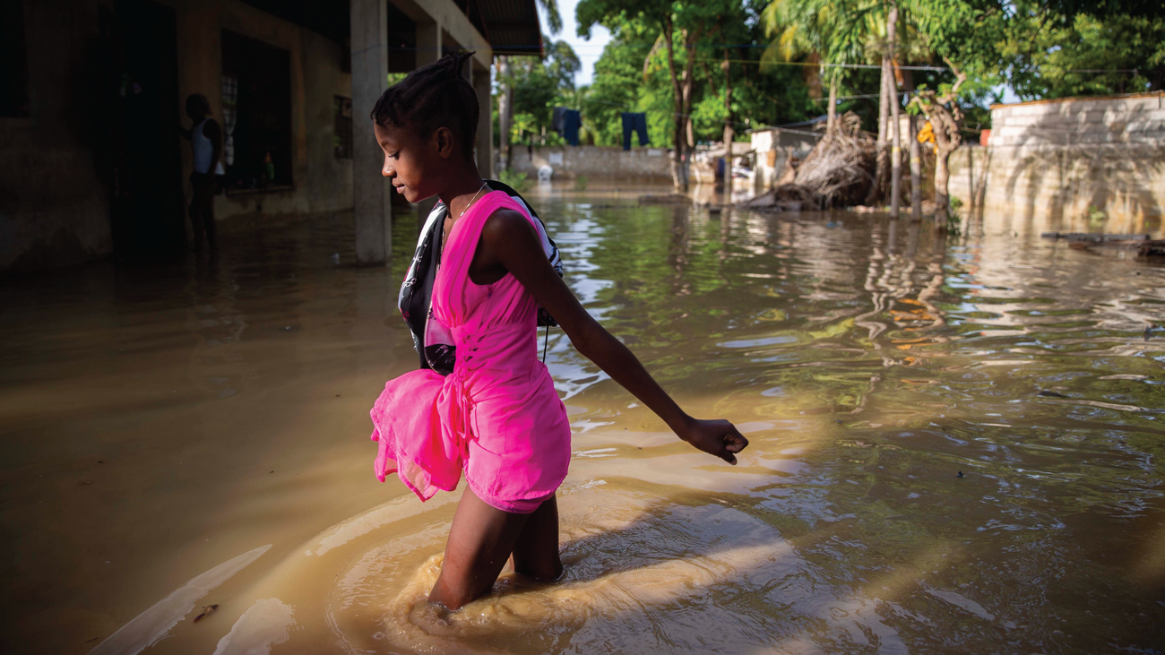 Girl in pink outfit wades through flood water in Haiti