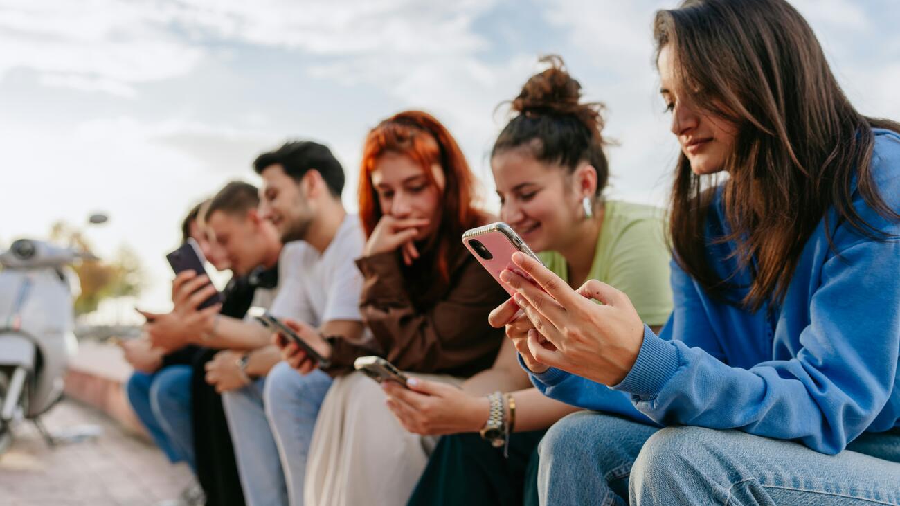 Young people sitting in a row outside looking at smartphones