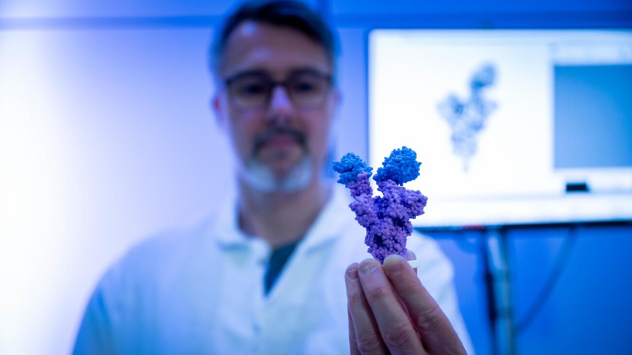 A person in a lab coat holding up a blue-violet crystalline structure