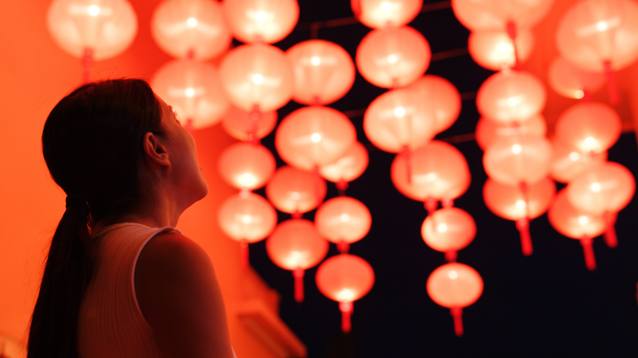 Side profile of a woman staring up at red lanterns that are glowing against the black sky