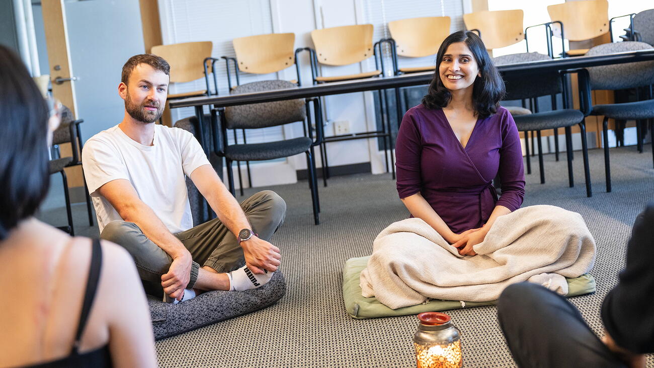 Dr. Varada Kolhatkar (right) seated cross-legged on a classroom floor, with other students seated in similar fashion