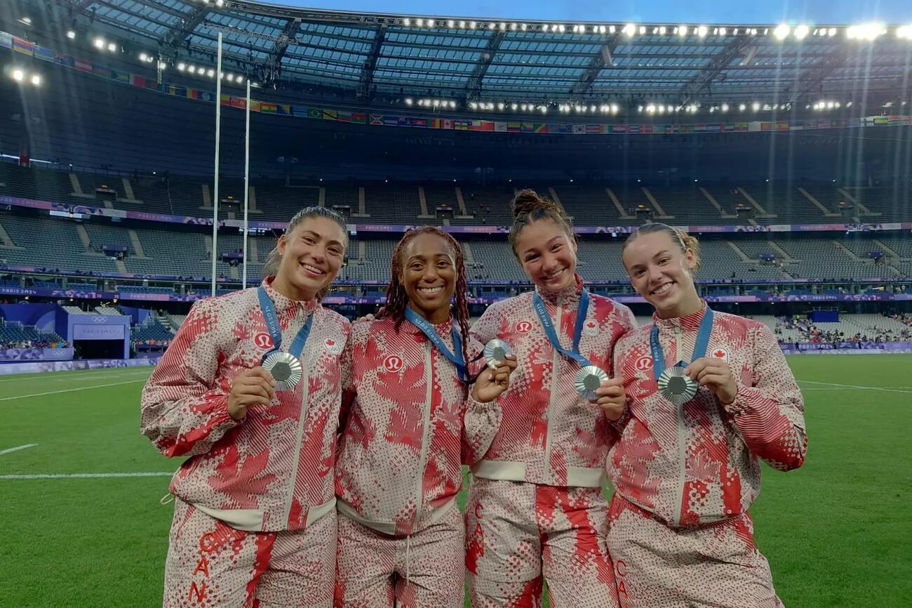 Four women athletes stand on field with their Olympic medals