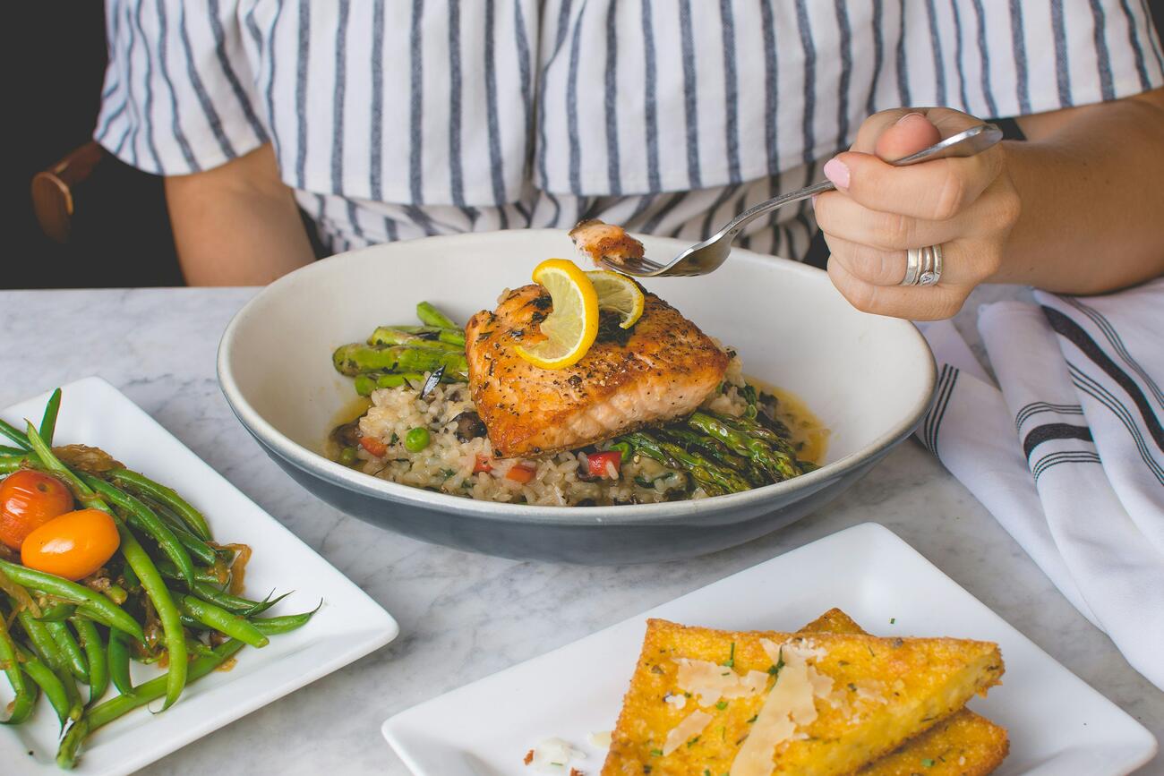 Person eating plate of salmon on asparagus and rice at table