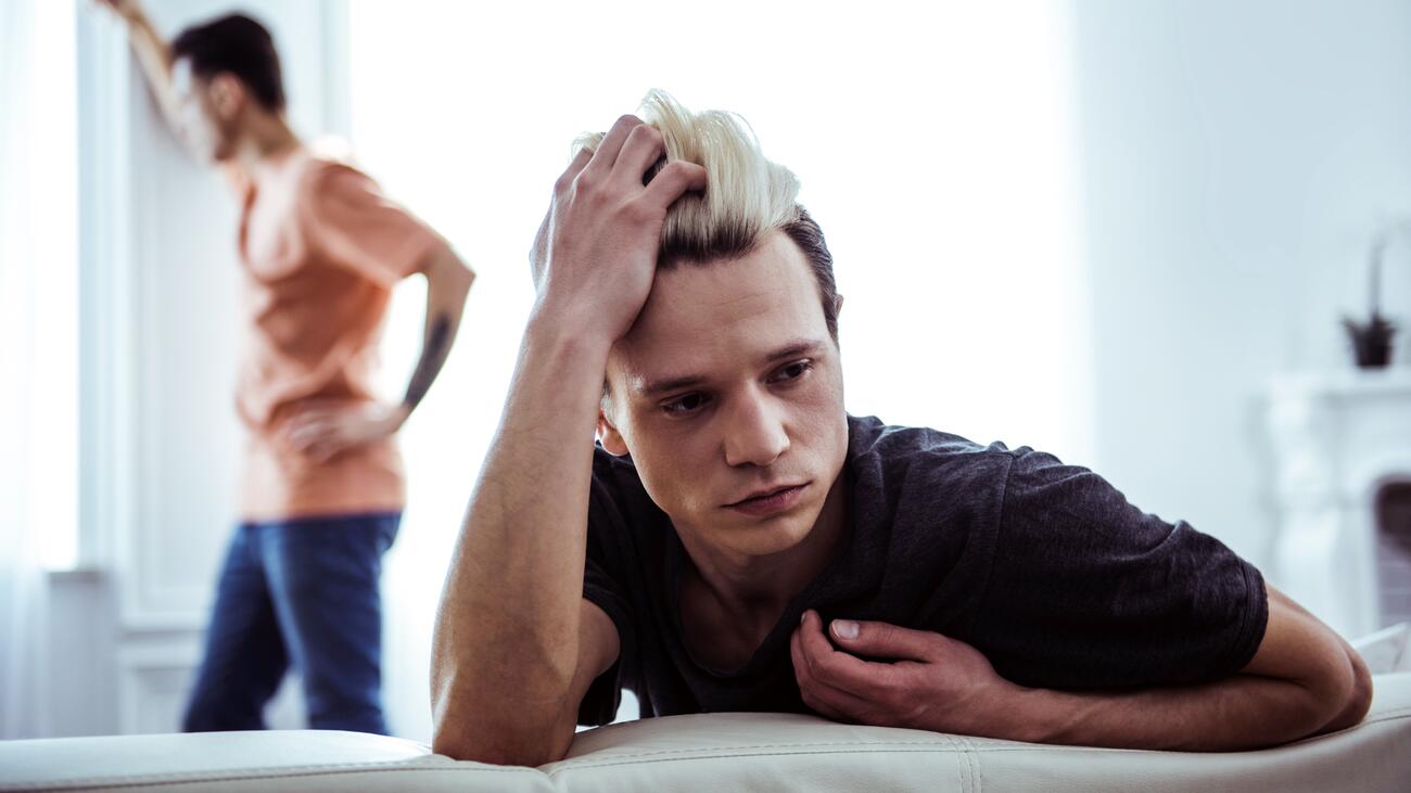 Stressed-out guy on couch looks away from man staring out window