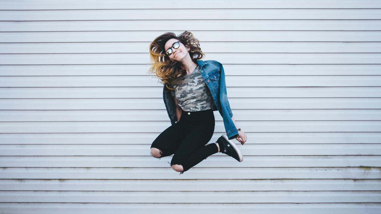 Woman in sunglasses jumping into air in front of wall