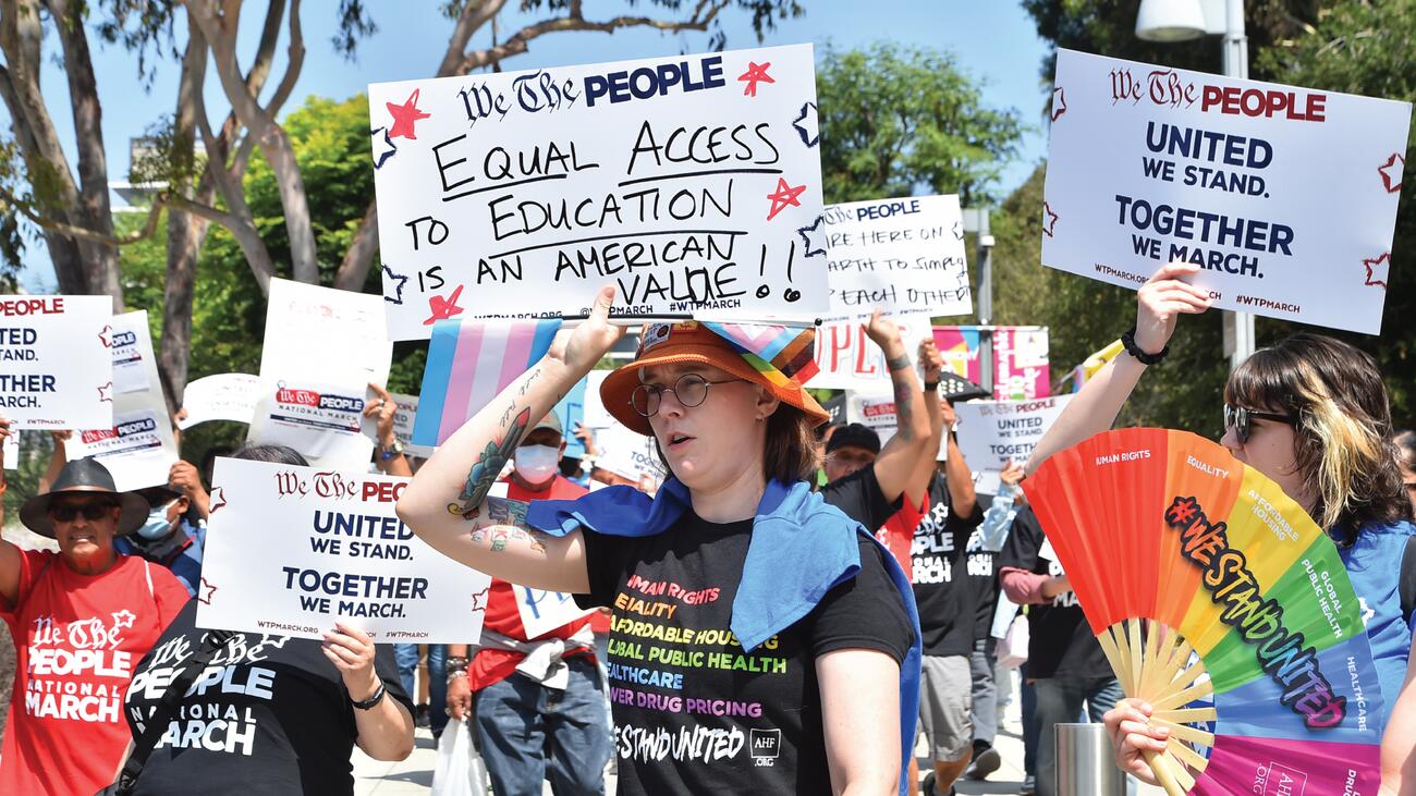 Protestors holding signs and displaying Pride rainbows