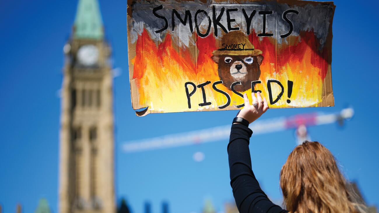 Woman holds wildfire protest sign at Canada's Parliament Hill