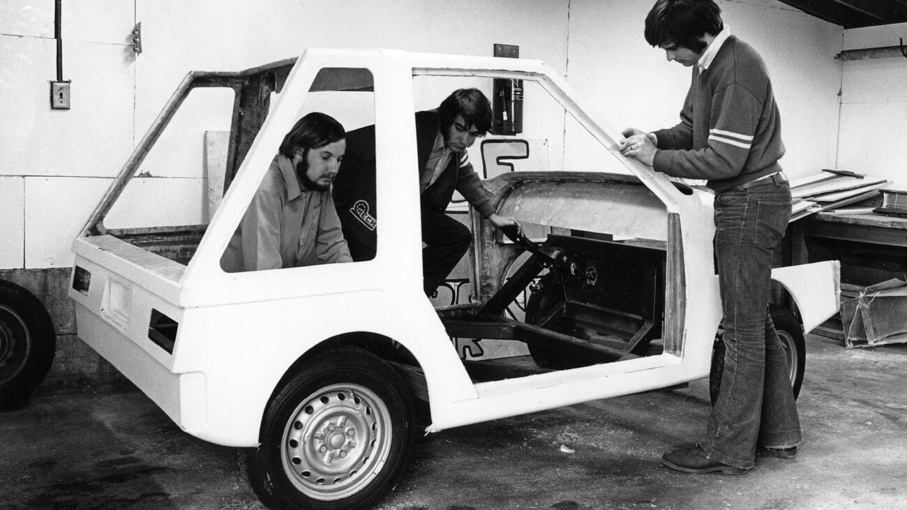 A black and white photo of three people working on the Wally Wagon