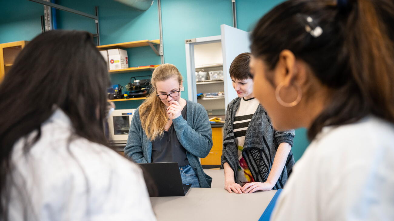 Three women gathered around fourth woman looking at laptop