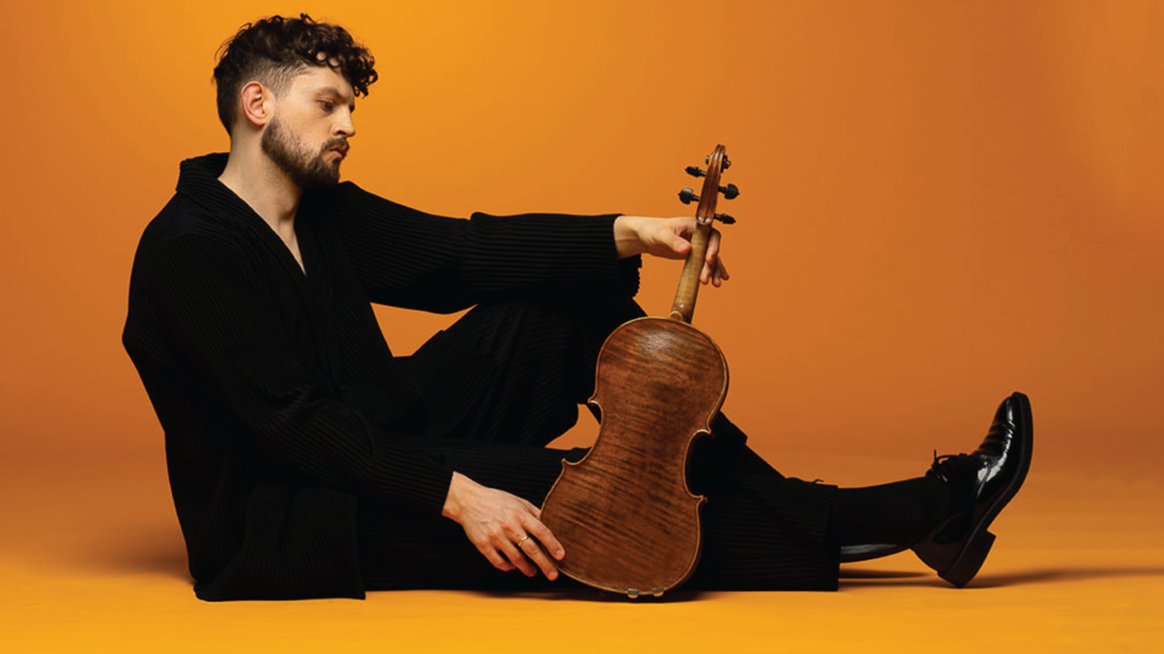 Man in black clothing sitting on ground with viola