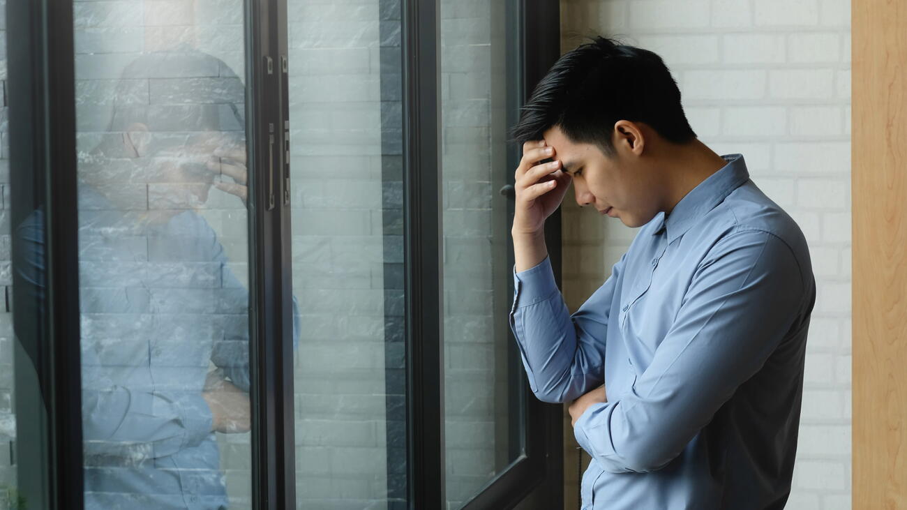 Man holds hand to forehead in front of windows