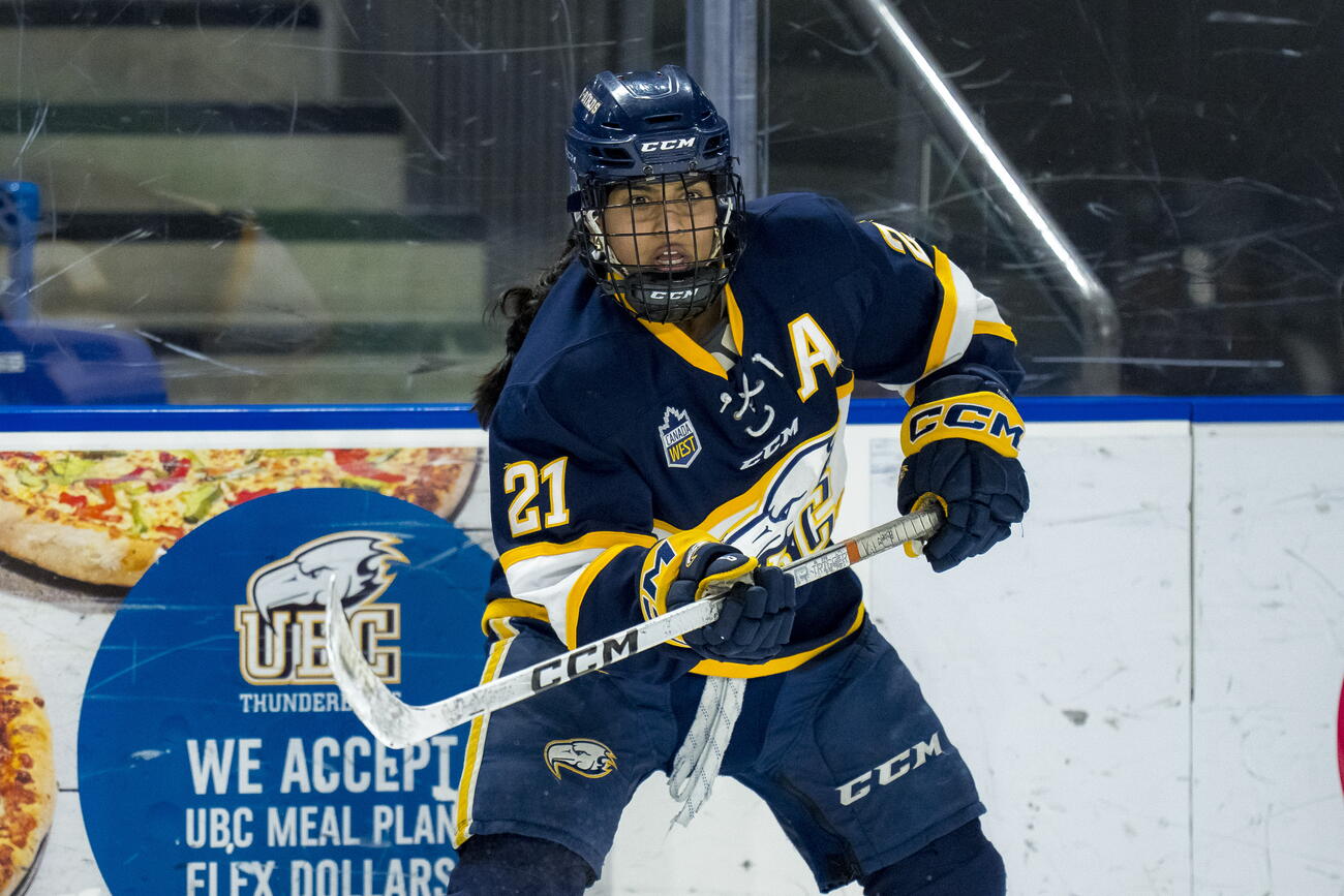 South Asian woman hockey player raises hockey stick on ice