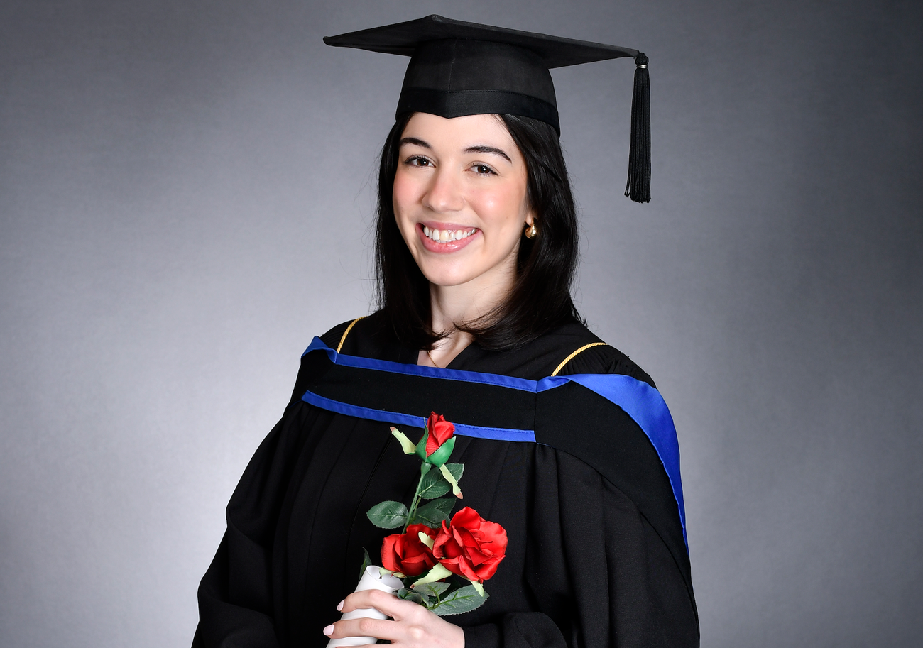Woman in graduation cap and gown carrying roses