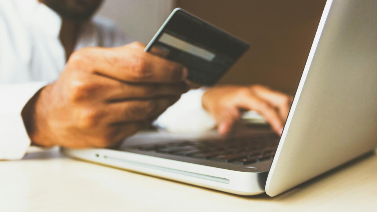 Man holds credit card while typing on laptop