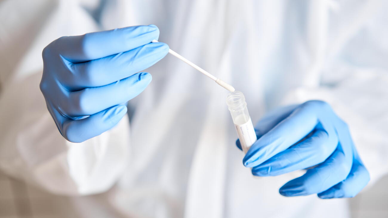 Lab worker in protective suit and gloves holds cotton swab over vial  