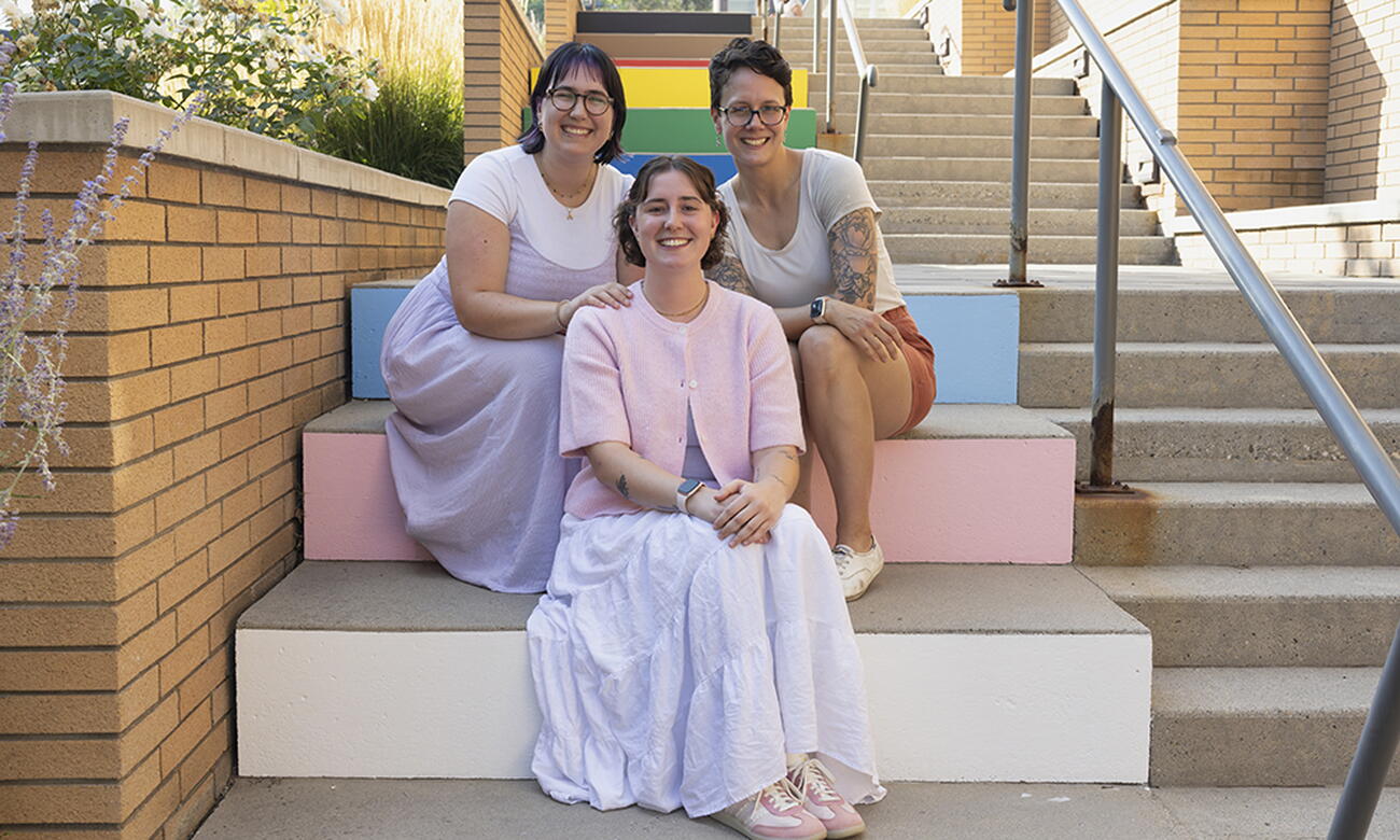 Three women sit on rainbow-coloured steps