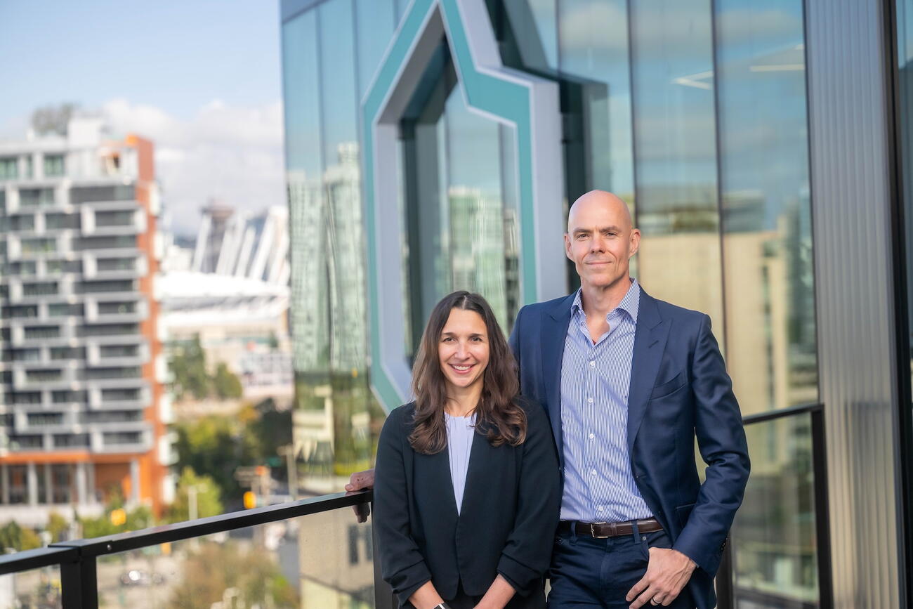 Woman and man stand by railing on balcony with buildings in background