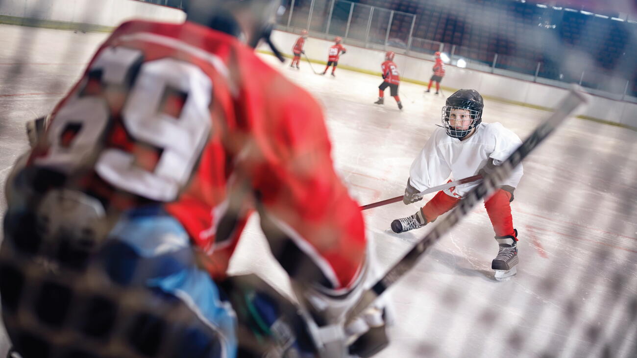 Young ice hockey player faces off against goalie in net