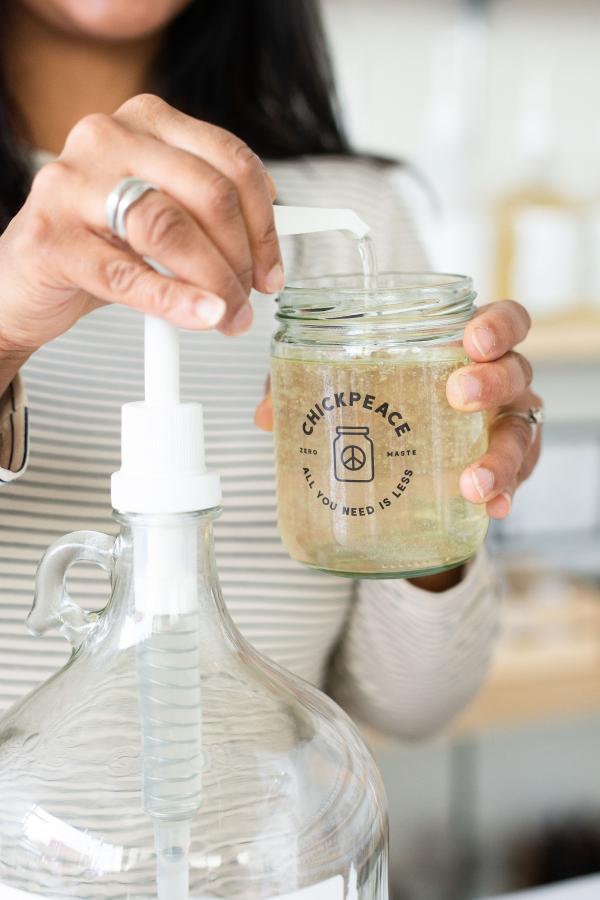Close-up image of Allisha's hands as she holds a glass jar while refilling it with liquid soap
