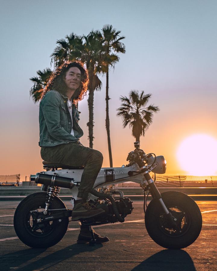 Cole Walliser on a motorcycle, with palm trees and the setting sun behind him