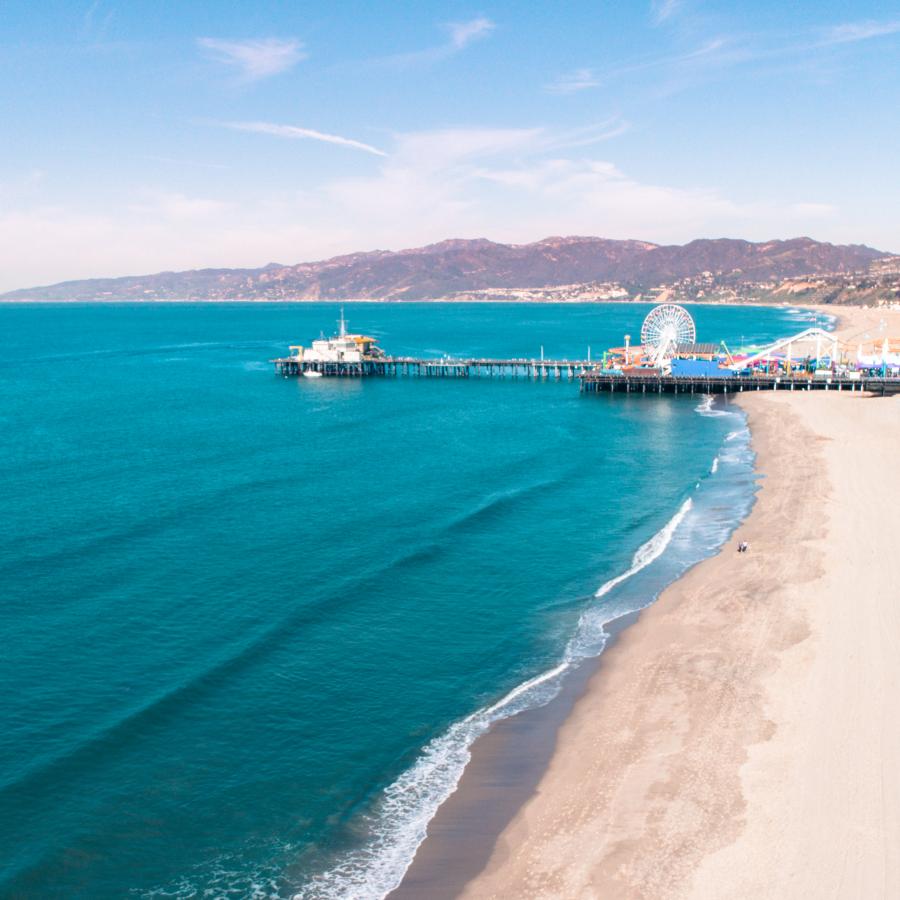 Wide angle shot of Santa Monica Pier, with the beach on the right and turquois-coloured water on the left
