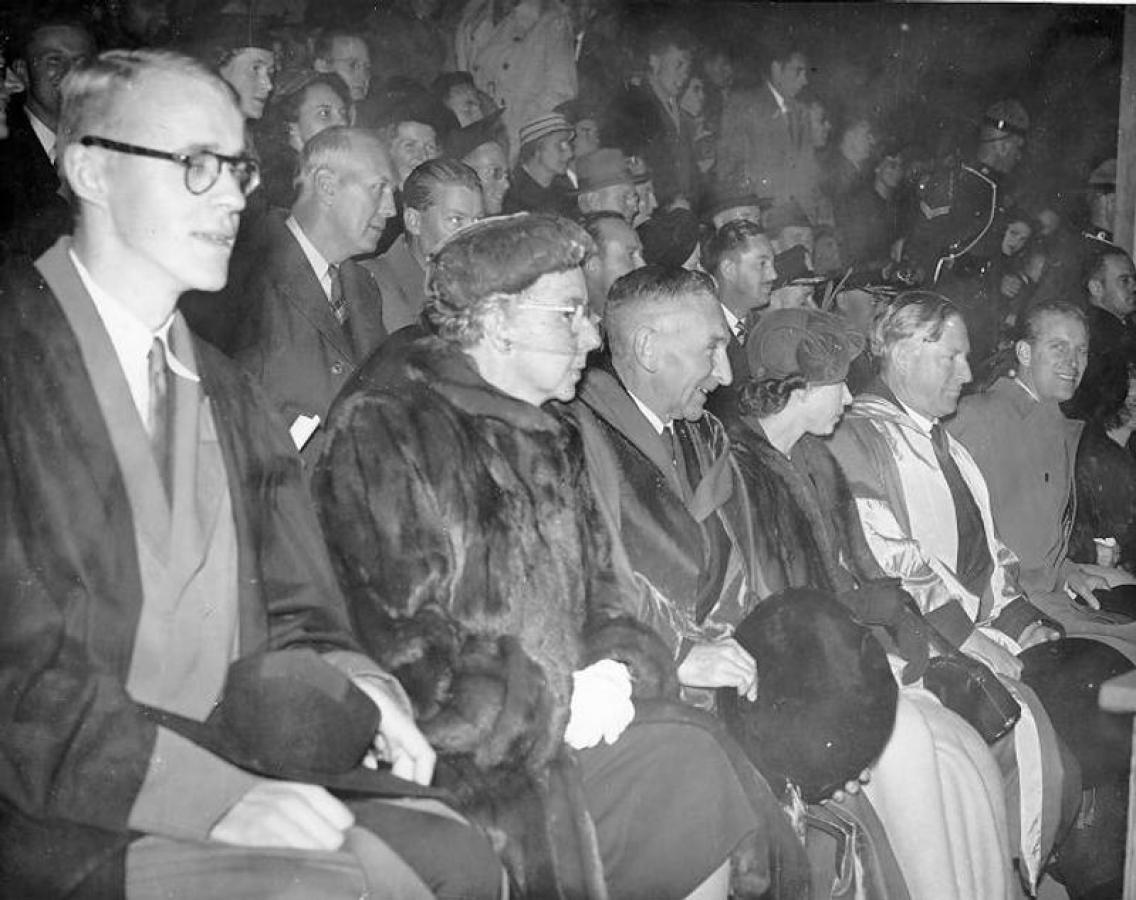 Princess Elizabeth, the Duke of Edinburgh, and N.A.M. MacKenzie seated at stadium