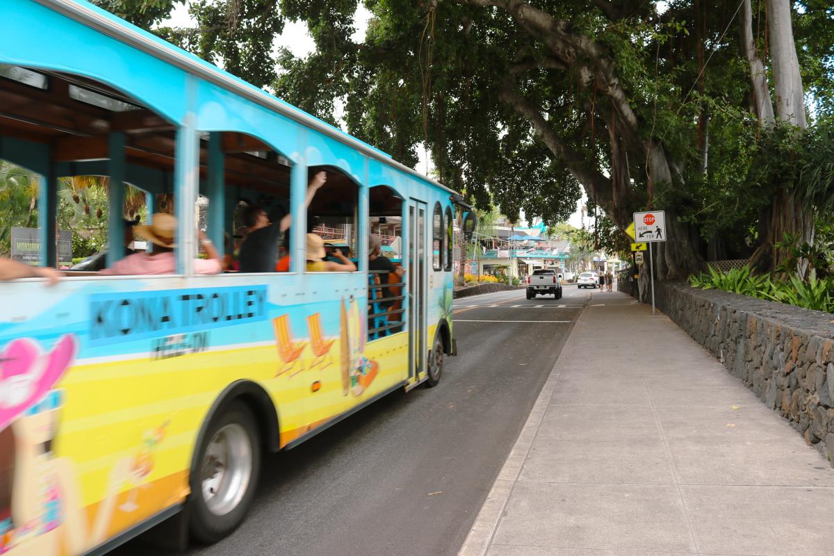 Shot of a road with a partially blurry image of the colourful Kona Trolley on the left