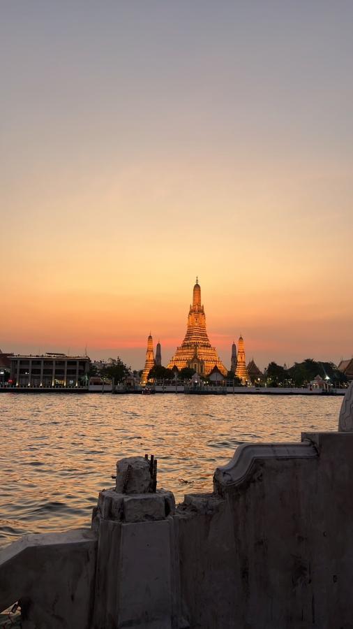 Wide-angle view of Wat Arun before dark, with water in the foreground