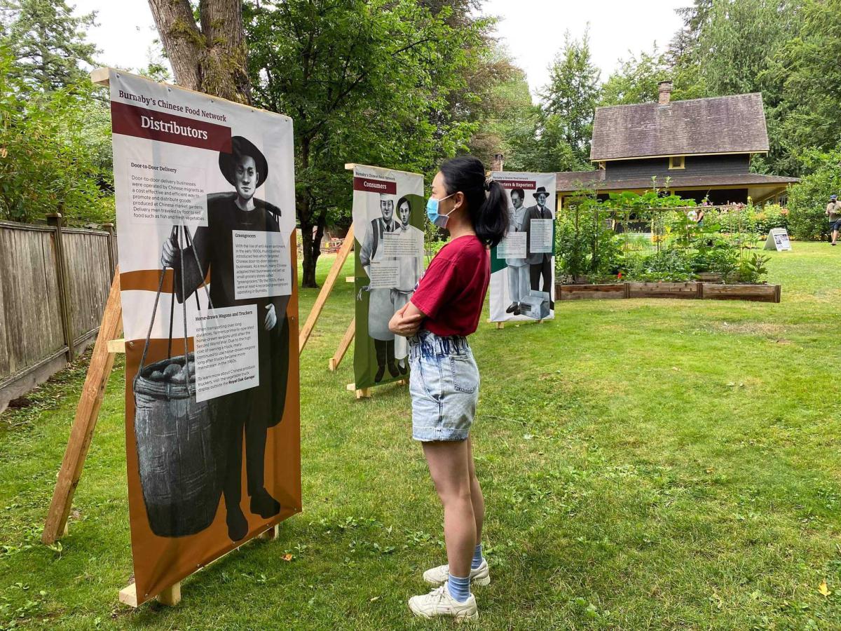 An Asian woman looks at an outdoor interpretive panel at the Burnaby Village Museum