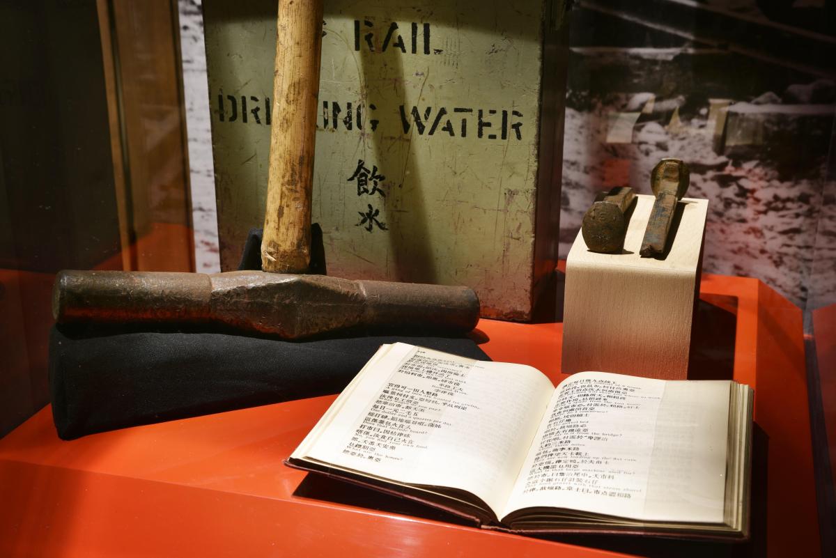 A close-up shot of an exhibit showing the steel head of a spike hammer, railroad spikes, and an open book
