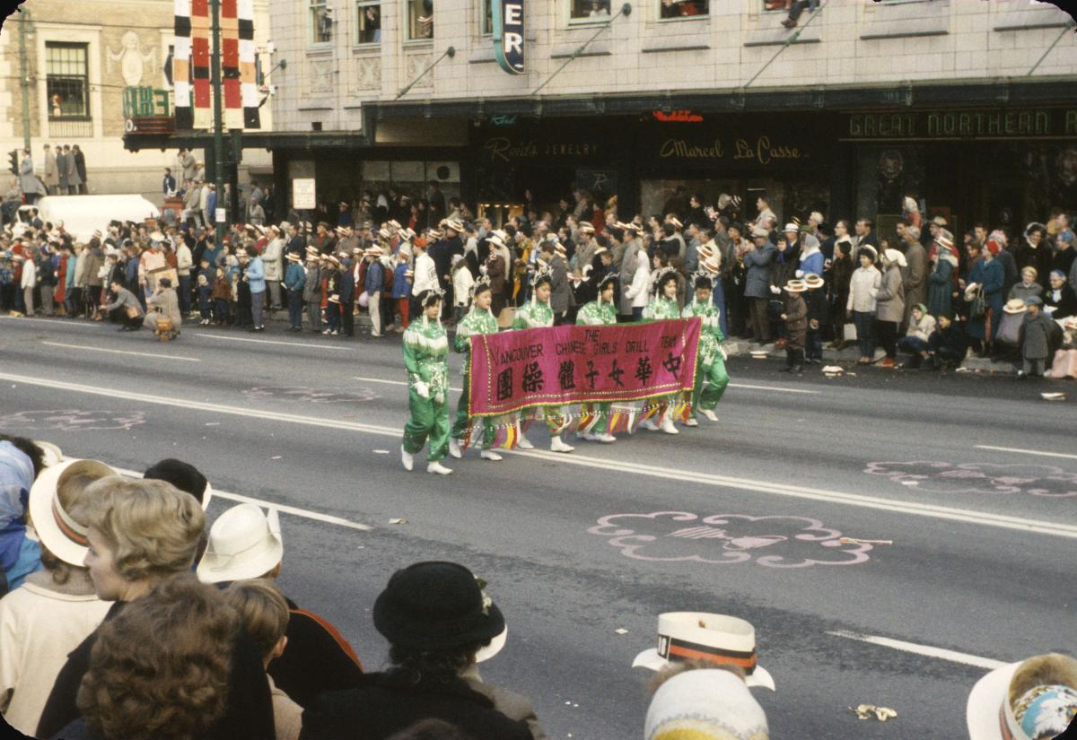 The Vancouver Chinese Girls' Drill Team marching on the street, carrying a banner with their name