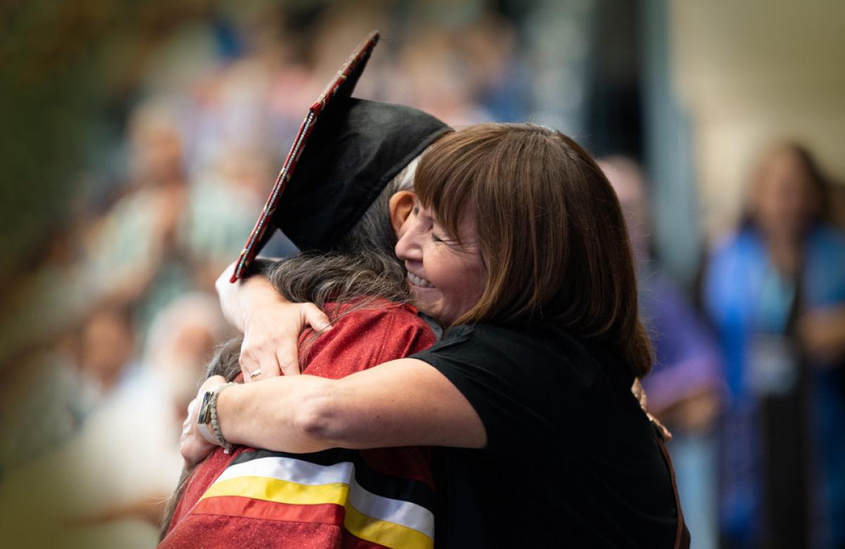 Two women (one in grad cap and gown) hugging at convocation ceremony