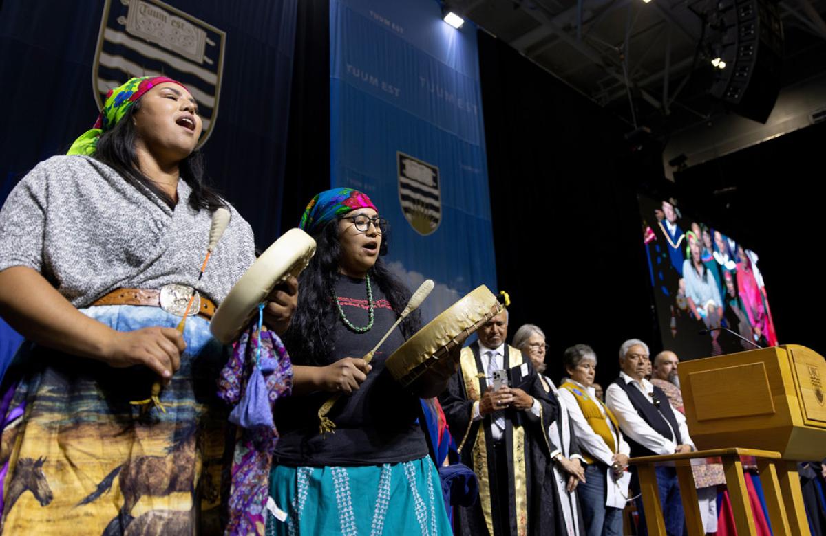 Two Indigenous performers with drums sing song at graduation ceremony