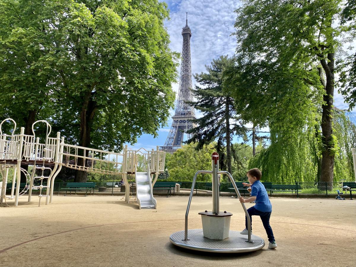 A playground surrounded by trees and showing the Eiffel Tower in the background