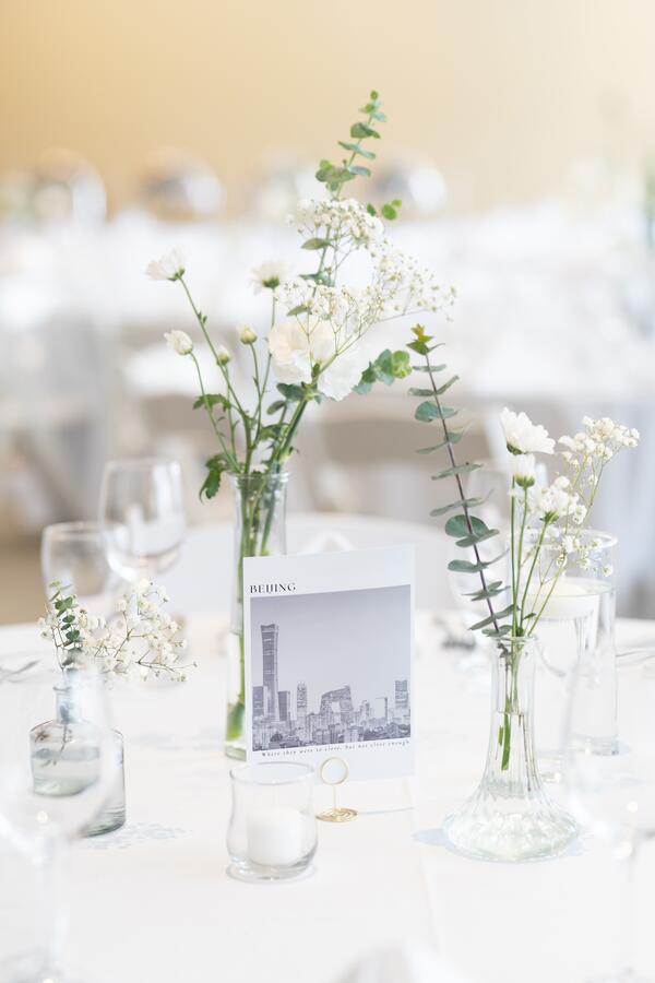 Wedding table decorated with clear vases, flowers, and a polaroid image of Beijing