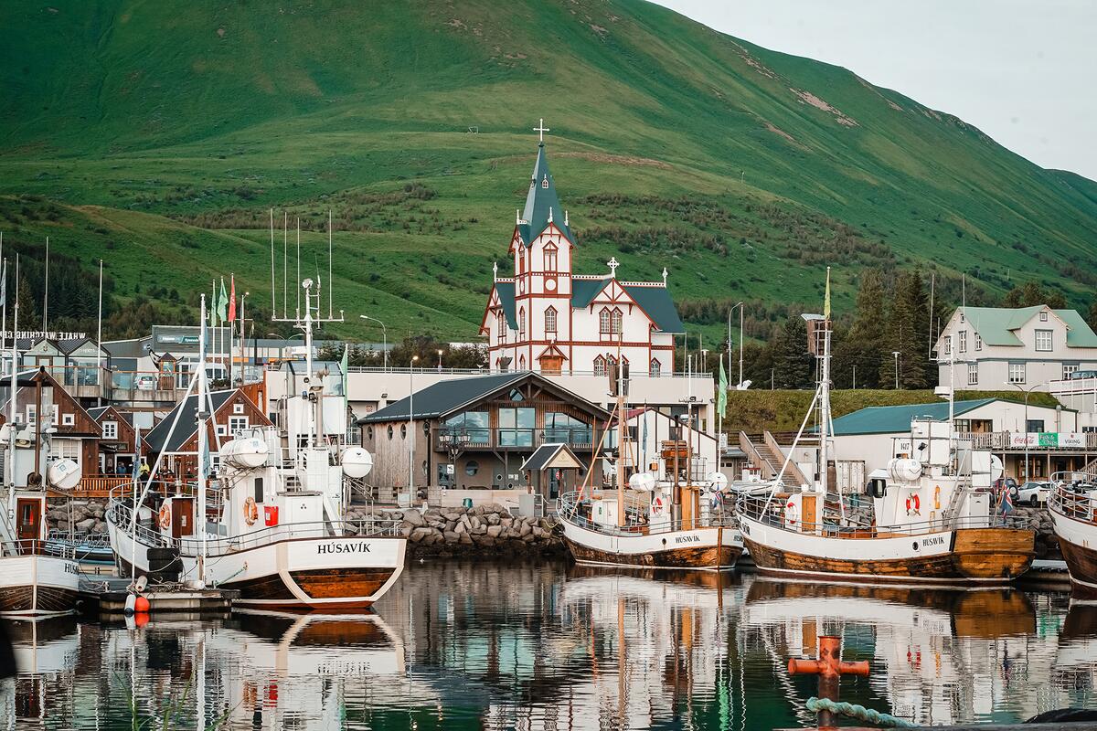 A view of Húsavík Church from the harbour, with Húsavík Mountain in the background and boats in the foreground