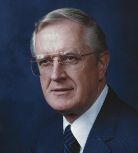 A headshot of George D. Cave with glasses, grey hair, and a navy suit.