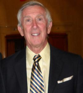 A headshot of James Craigen, who is wearing a black suit and striped tie.